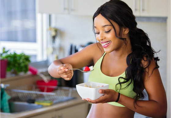A photo of a woman eating a strawberry out of a ceramic bowl.